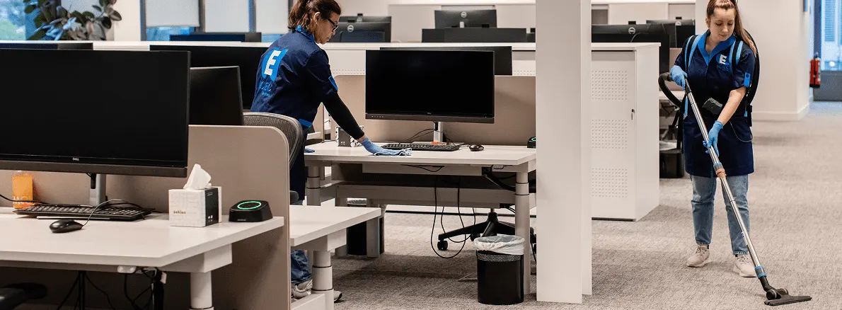 Deux agentes NCIEC en tenue bleue nettoient les postes de travail d’un open space