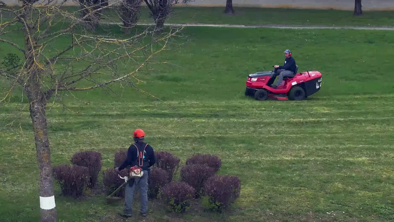 Jardinier NCIEC taillant des massifs pendant qu'un collègue tond une grande pelouse