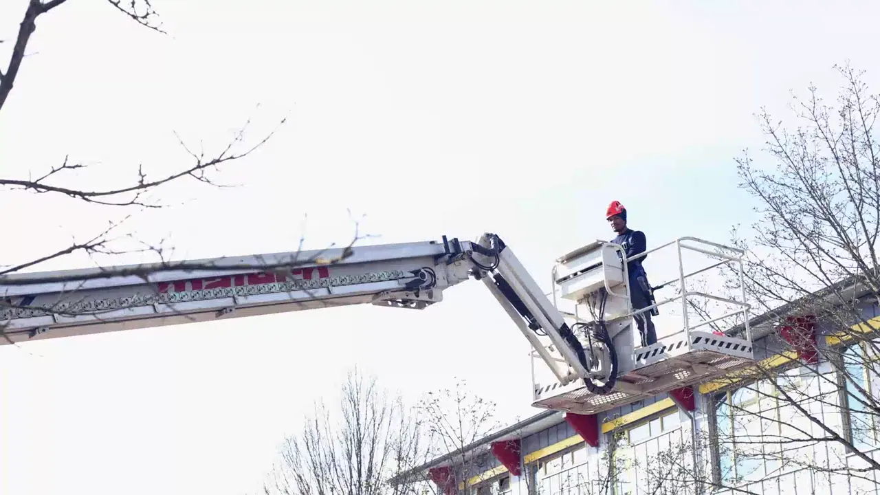 Technicien NCIEC sur une nacelle élévatrice devant la façade vitrée d’un immeuble